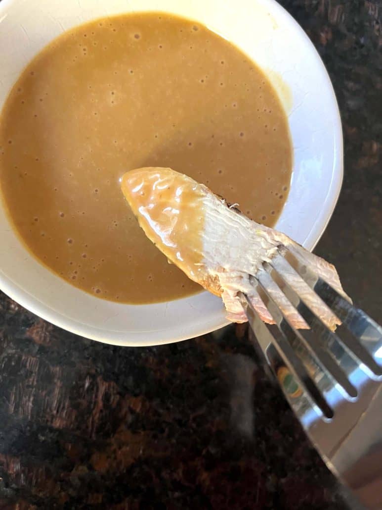 A piece of chicken dipped in homemade Chick-Fil-A sauce held by a fork.