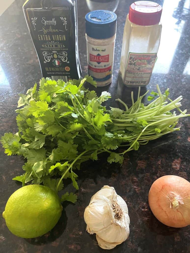 Ingredients for Cilantro Chimichurri. Fresh cilantro, a lime, garlic, a small onion, extra virgin olive oil, salt, and pepper, ready to be blended into a flavorful sauce