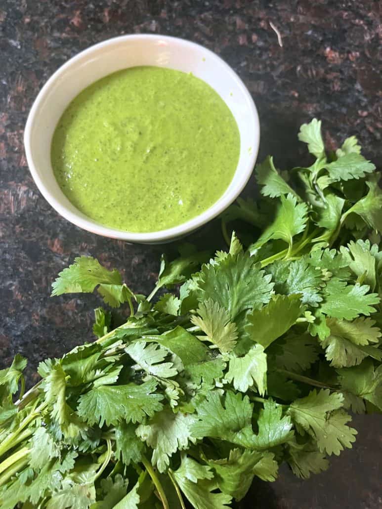 A bowl filled with green Cilantro Chimichurri sauce next to a bunch of fresh cilantro, highlighting the main ingredient of this flavorful sauce.