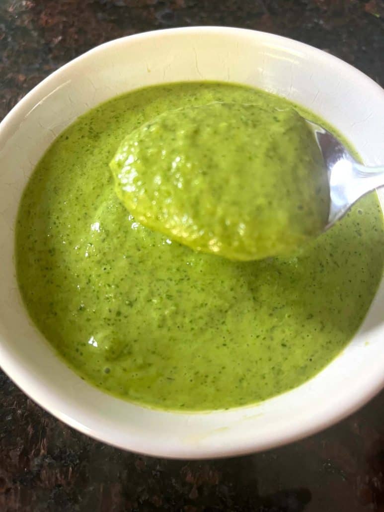 Close-up of a spoon lifting a thick, vibrant green Cilantro Chimichurri sauce from a bowl, showcasing its creamy and smooth texture.