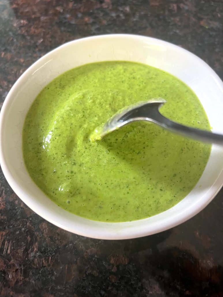 A spoon dipped into a bowl of Cilantro Chimichurri sauce, highlighting its smooth and creamy consistency.