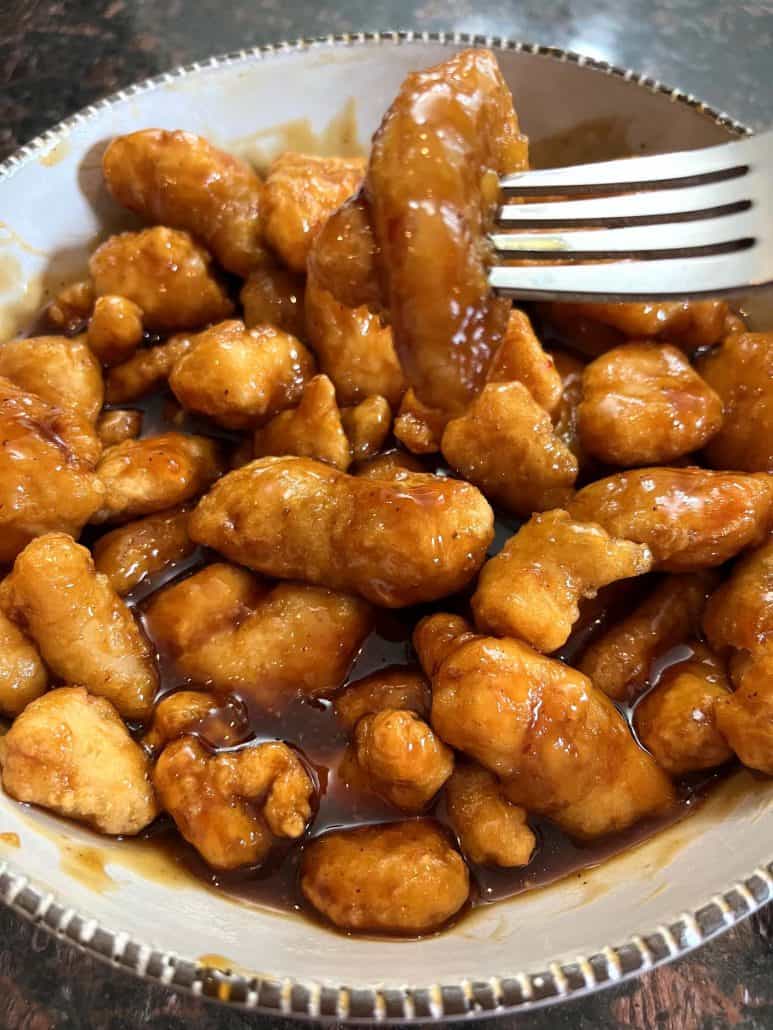 A close-up of a bowl of cooked General Tso’s chicken, with a fork lifting a saucy, crispy piece, showing the golden coating and rich sauce after being air-fried.