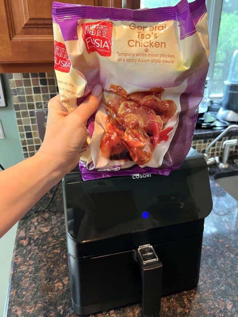 Melanie Mendelson from melaniecooks.com holds a bag of frozen General Tso’s chicken in front of an air fryer.