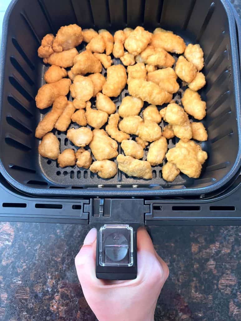 Melanie Mendelson from melaniecooks.com holds an air fryer basket filled with frozen General Tso’s chicken pieces, arranged in a single layer.