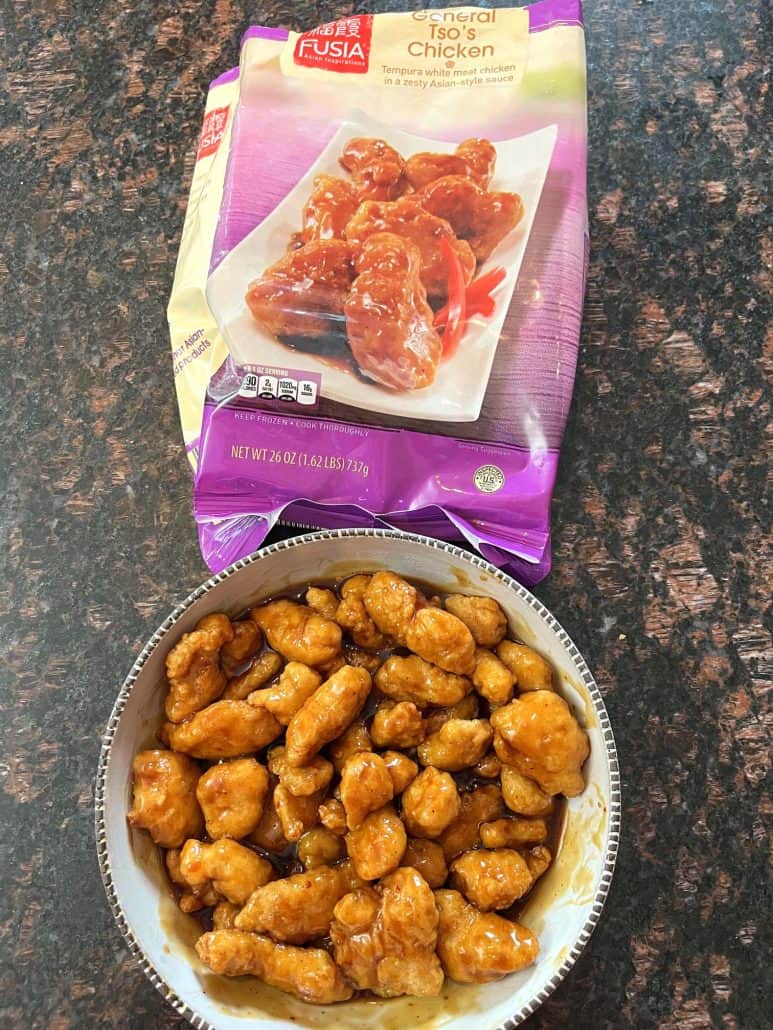  A bowl of cooked General Tso’s chicken is placed in front of the package of the frozen product,