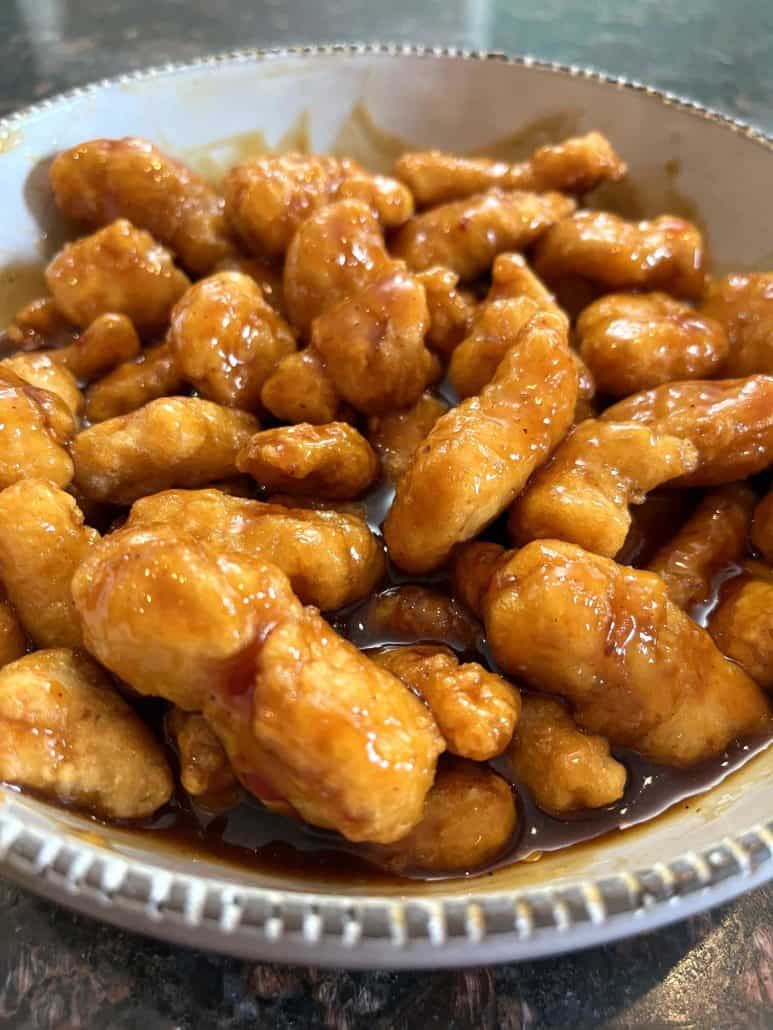 A bowl of air-fried General Tso’s chicken coated in a rich, glossy sauce, showcasing the crispy texture of the chicken and the flavorful coating after cooking.