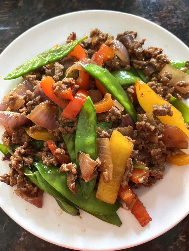 A plate filled with freshly made Ground Beef Stir Fry, featuring a colorful mix of red and yellow bell peppers, snow peas, red onions, and seasoned ground beef. 