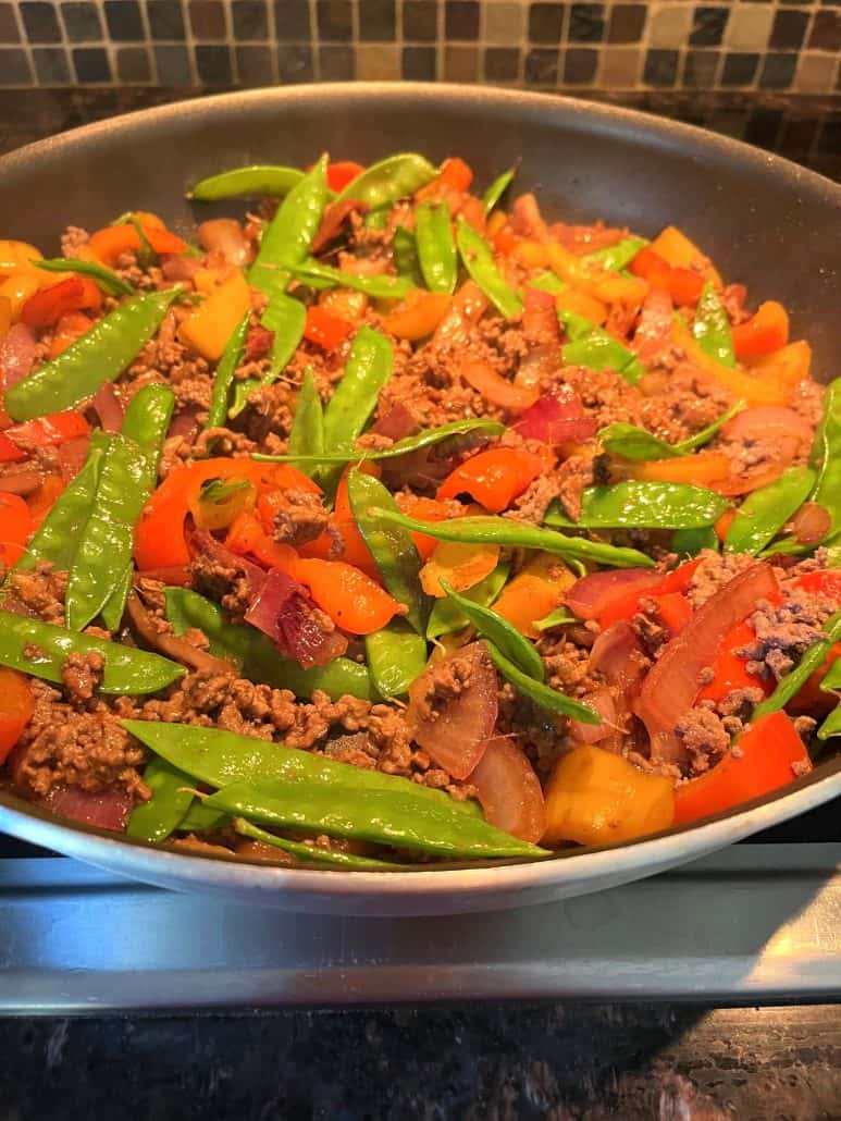 A skillet filled with Ground Beef Stir Fry, featuring a vibrant array of ingredients including snow peas, red and yellow bell peppers, and red onions, all mixed with savory ground beef.