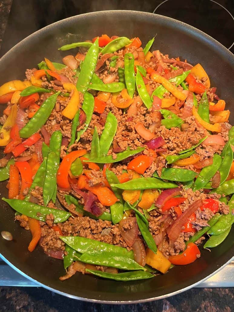 A top-down view of a skillet filled with a freshly made Ground Beef Stir Fry, featuring a colorful combination of ground beef, snow peas, red onions, and red and yellow bell peppers.