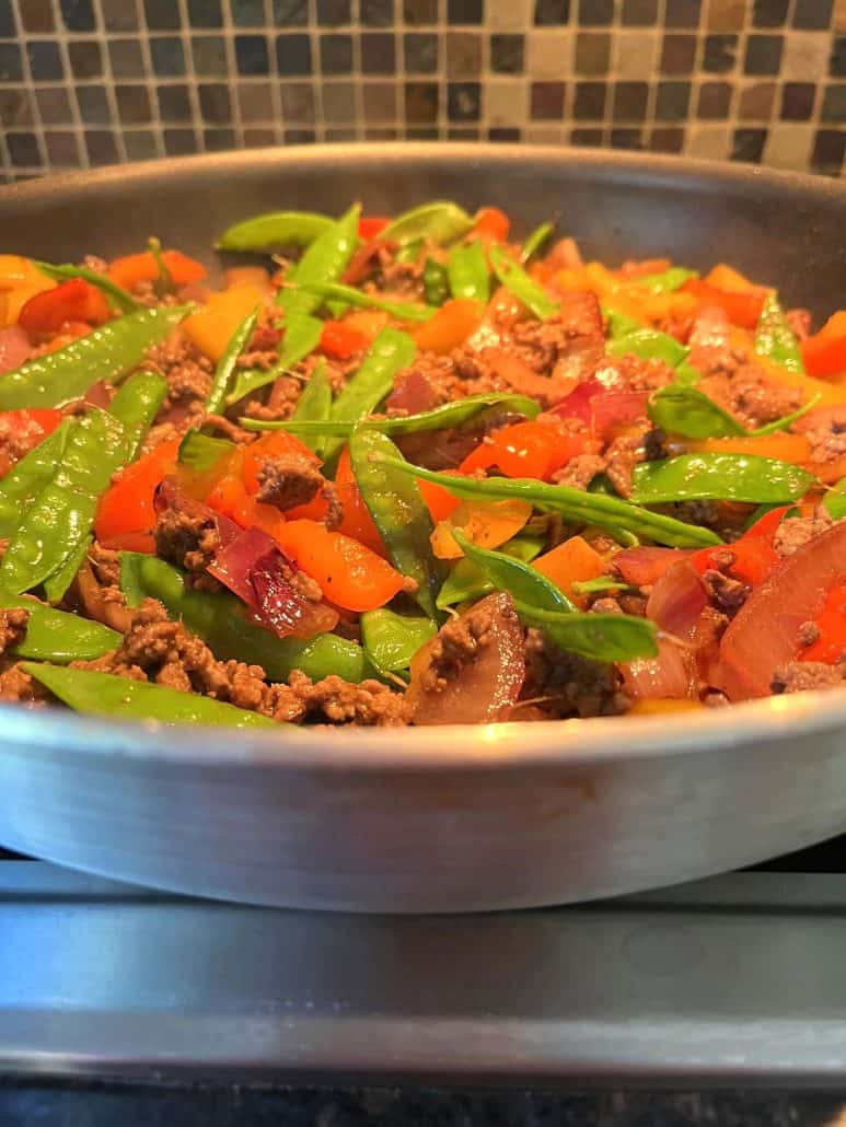 A side view of a skillet filled with Ground Beef Stir Fry, showcasing a colorful blend of ground beef, snow peas, red onions, and bell peppers.