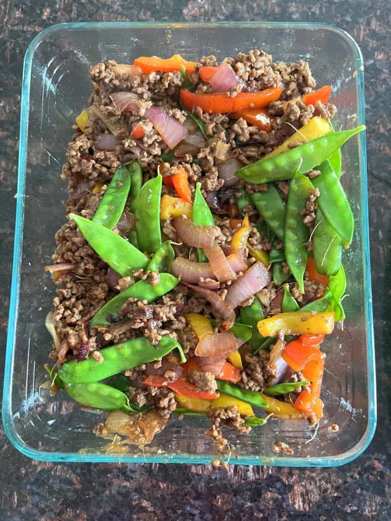 A glass container filled with freshly prepared Ground Beef Stir Fry, featuring a colorful mix of red and yellow bell peppers, snow peas, red onions, and seasoned ground beef. 