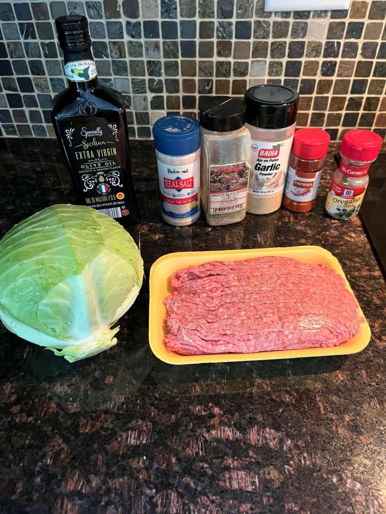 Ingredients for Ground Turkey and Cabbage laid out on a kitchen counter, including a head of cabbage, ground turkey, olive oil, and various seasonings like salt, pepper, garlic powder, paprika, and oregano, ready for a quick and healthy meal.