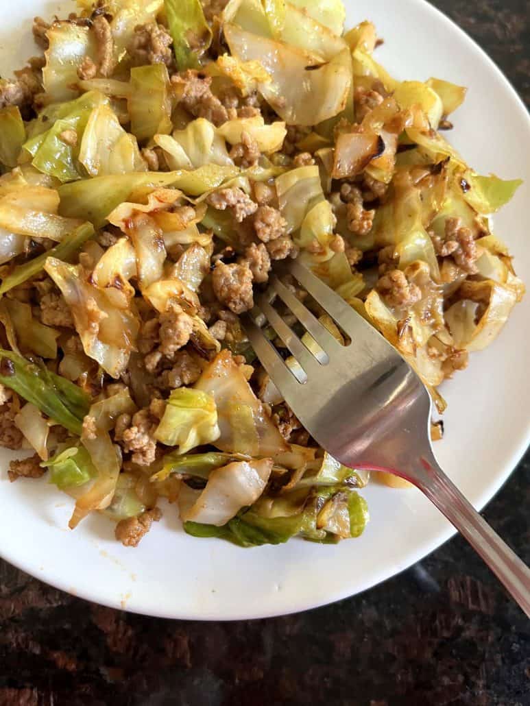 A fork resting on a plate of ground turkey and sautéed cabbage.