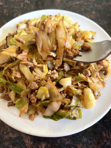 A fork lifting a bite of ground turkey and sautéed cabbage from a plate.