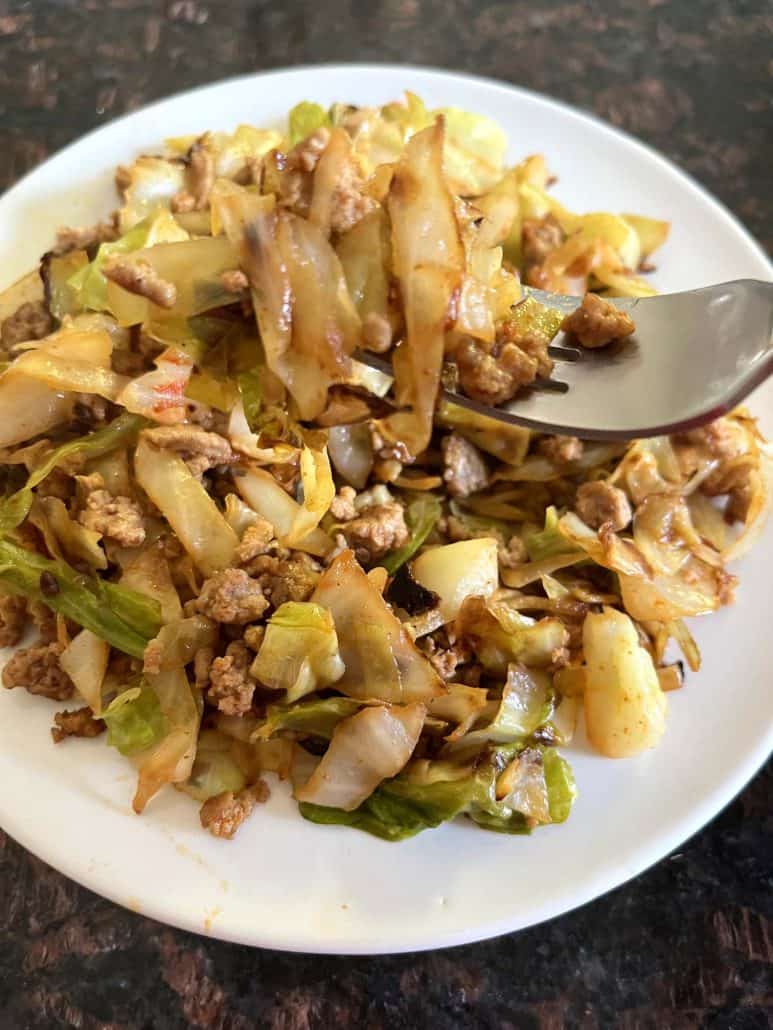 A fork lifting a bite of ground turkey and sautéed cabbage from a plate.