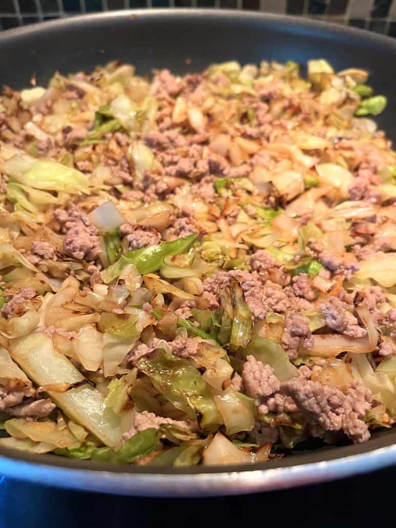 A spoonful of sautéed cabbage and ground turkey lifted from the pan.