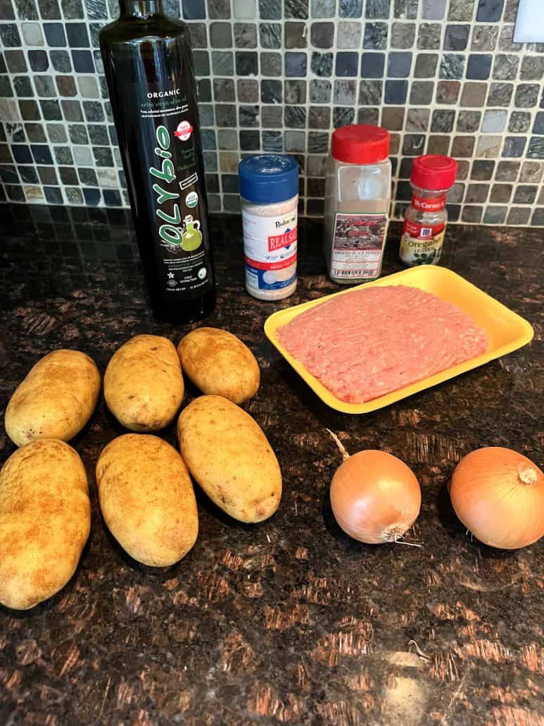 Ingredients for a ground turkey and potato skillet meal, including potatoes, ground turkey, onions, olive oil, salt, pepper, and oregano,