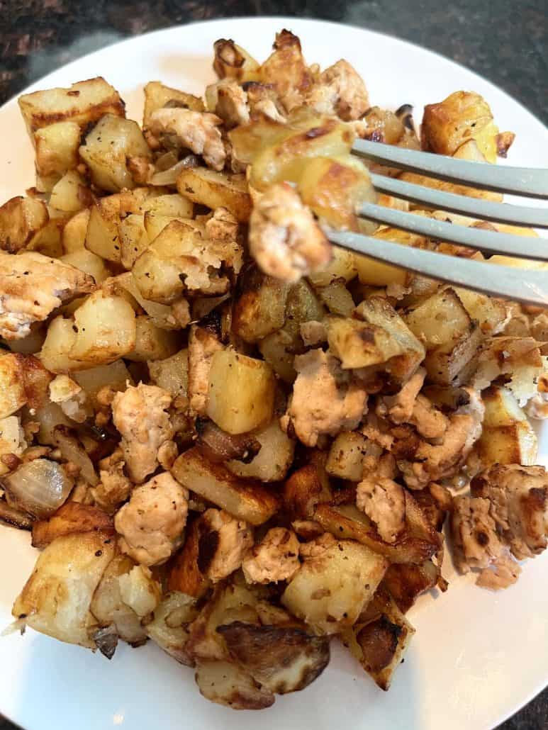 A fork lifting a bite of crispy diced potatoes and ground turkey from a plate, ready to be enjoyed.