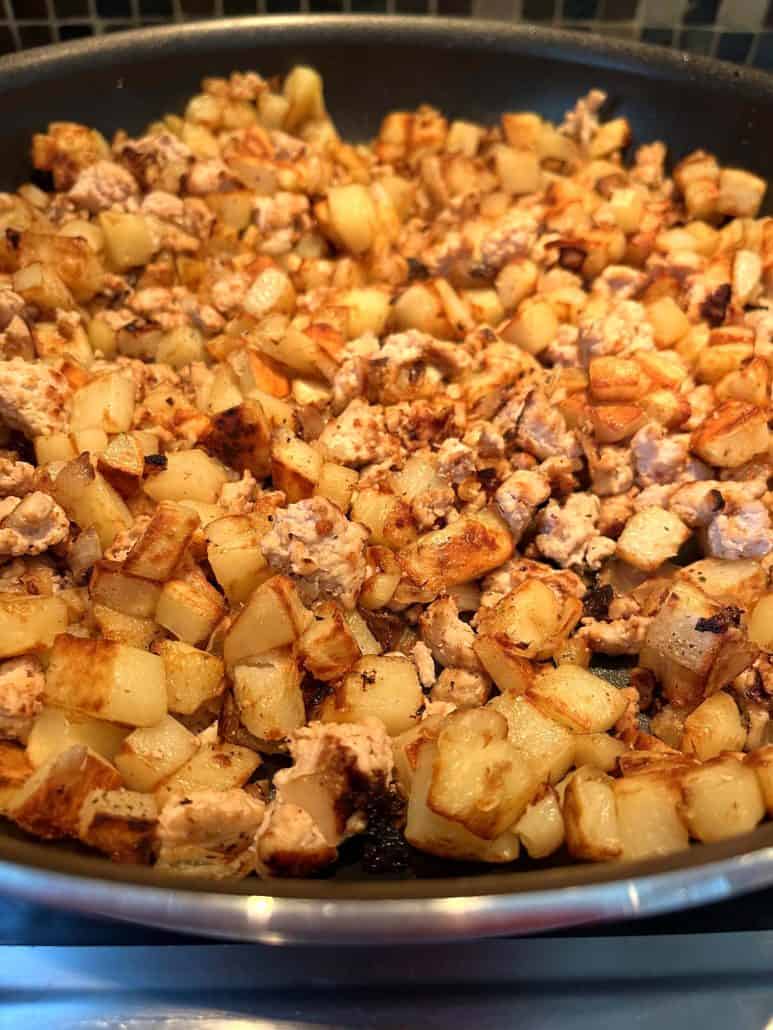 Close-up of golden-brown diced potatoes and ground turkey cooking in a skillet, highlighting the crispy and tender texture of the ingredients.