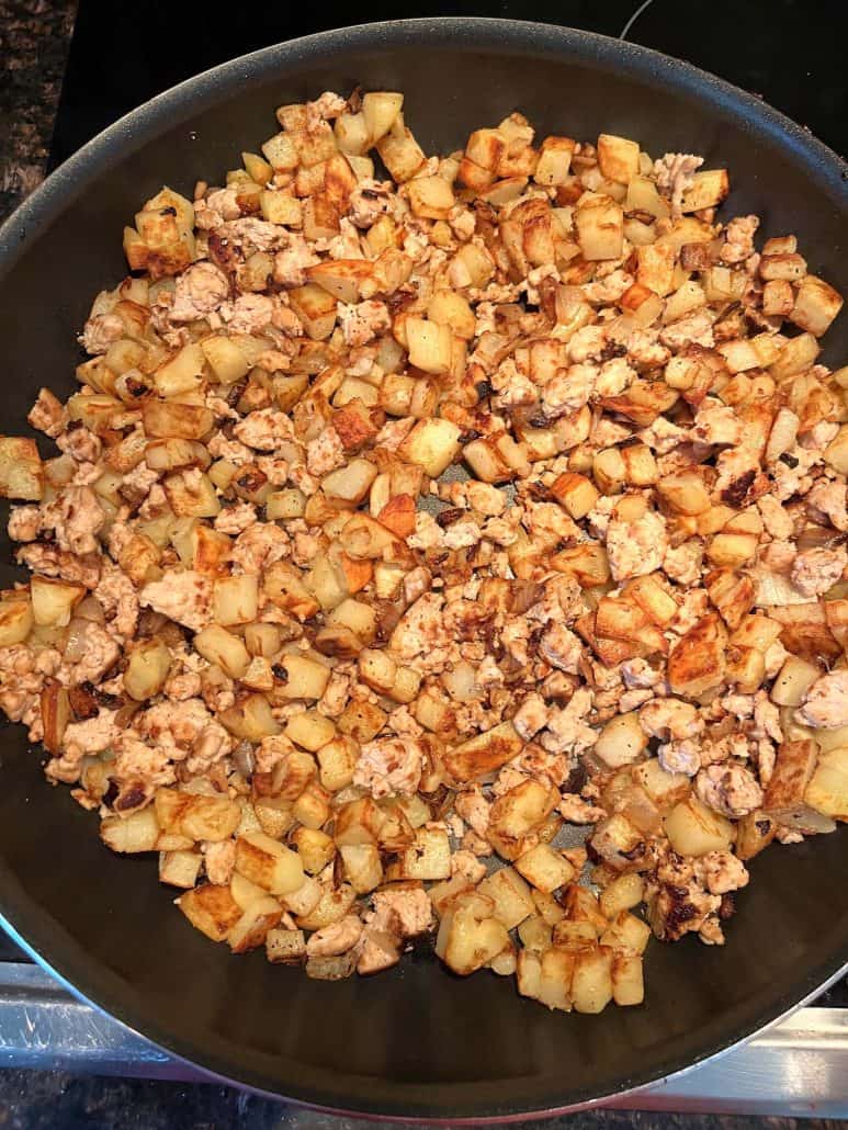 Top view of a skillet filled with evenly browned diced potatoes and ground turkey.