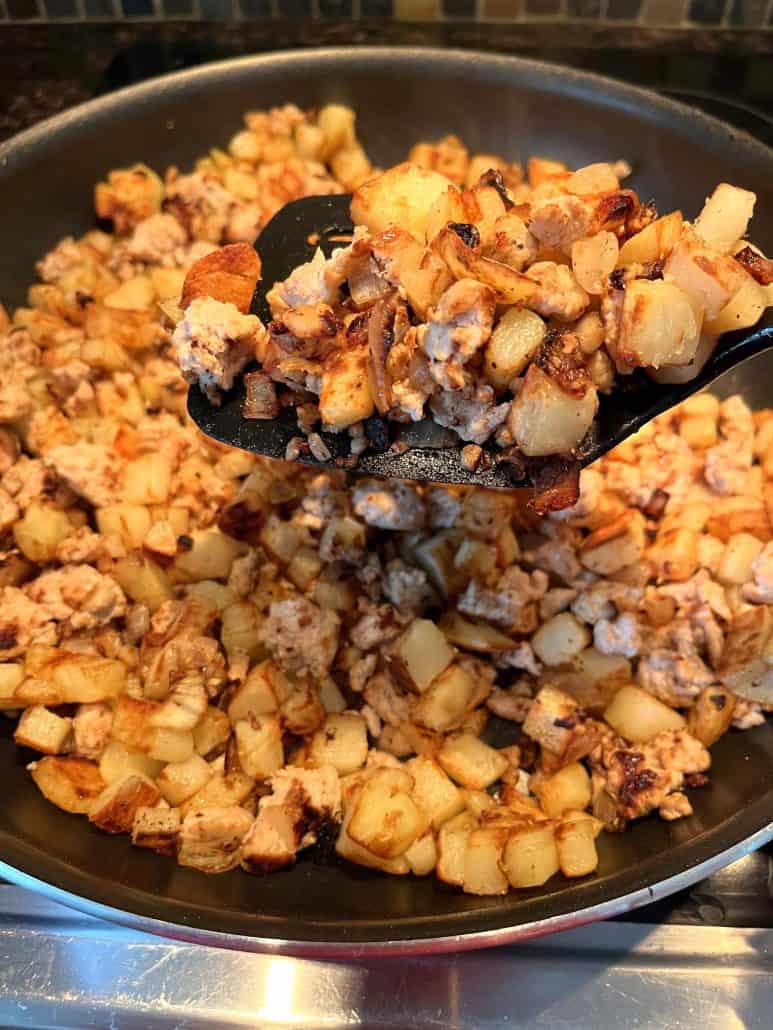 A close-up of a spatula lifting a portion of browned diced potatoes and ground turkey from a skillet.