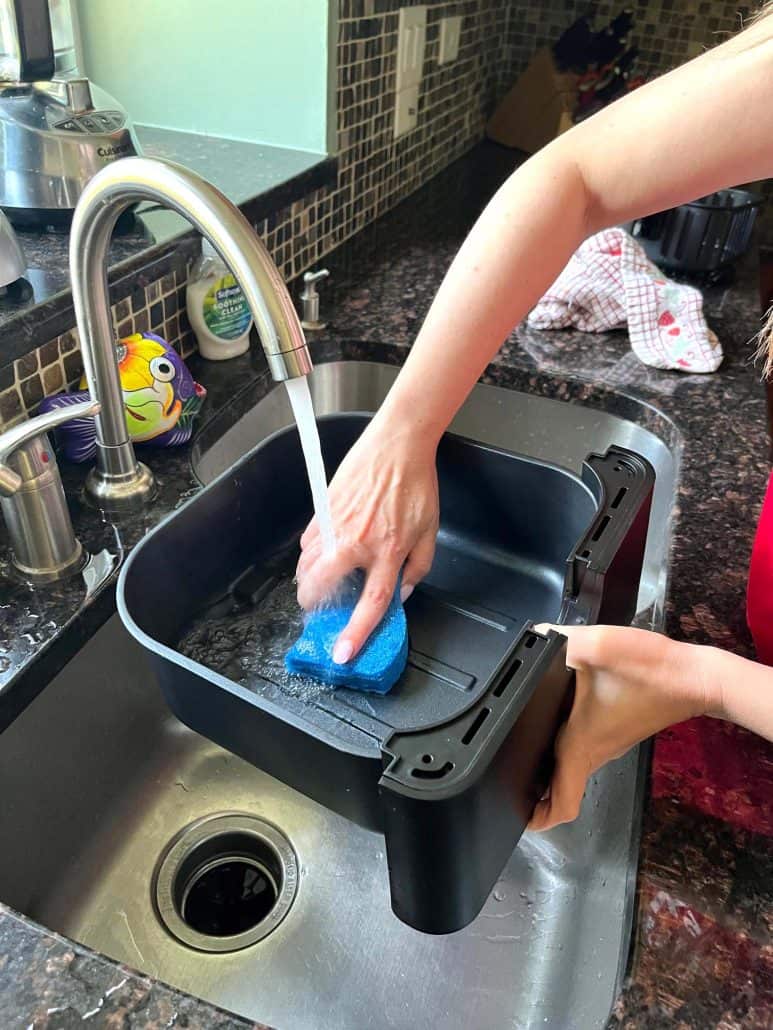 Cleaning the outer basket of air fryer by hand, using a soft sponge to avoid damaging the non-stick surface.