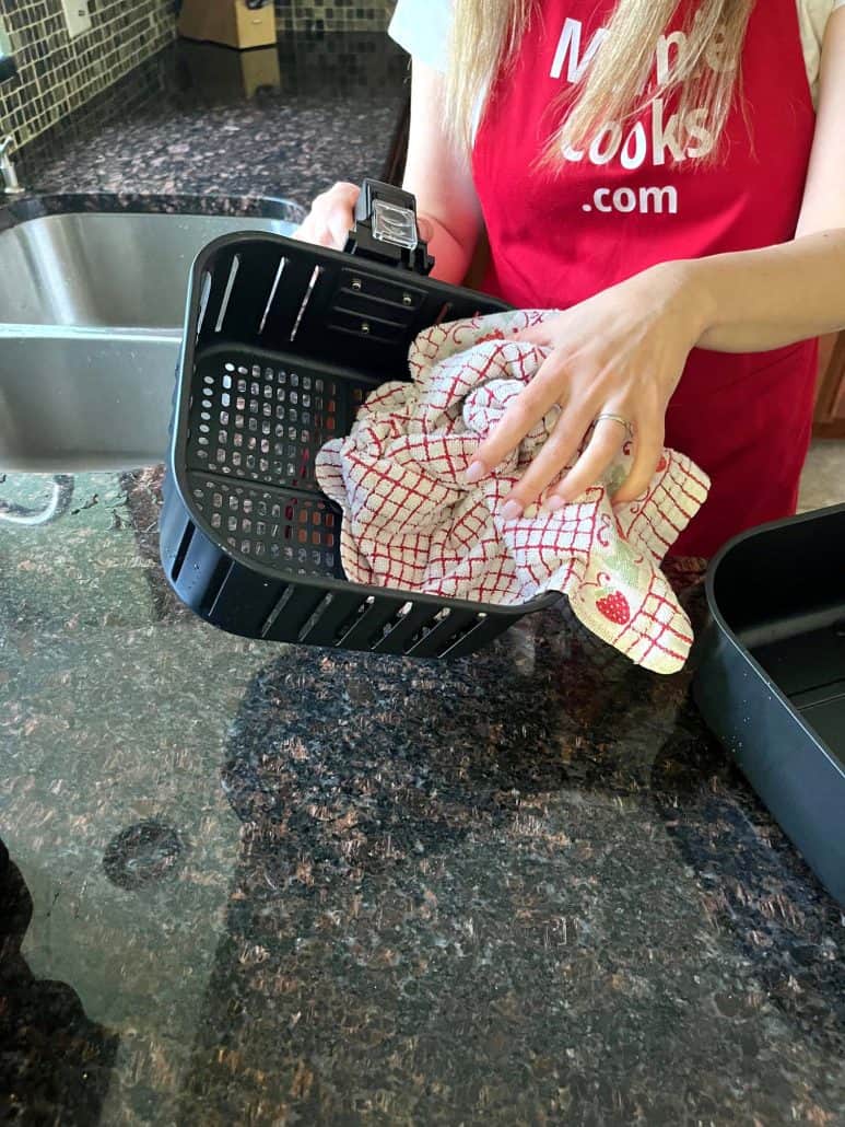 Drying the inner basket of a Cosori air fryer with a towel after washing, ensuring it's completely dry.