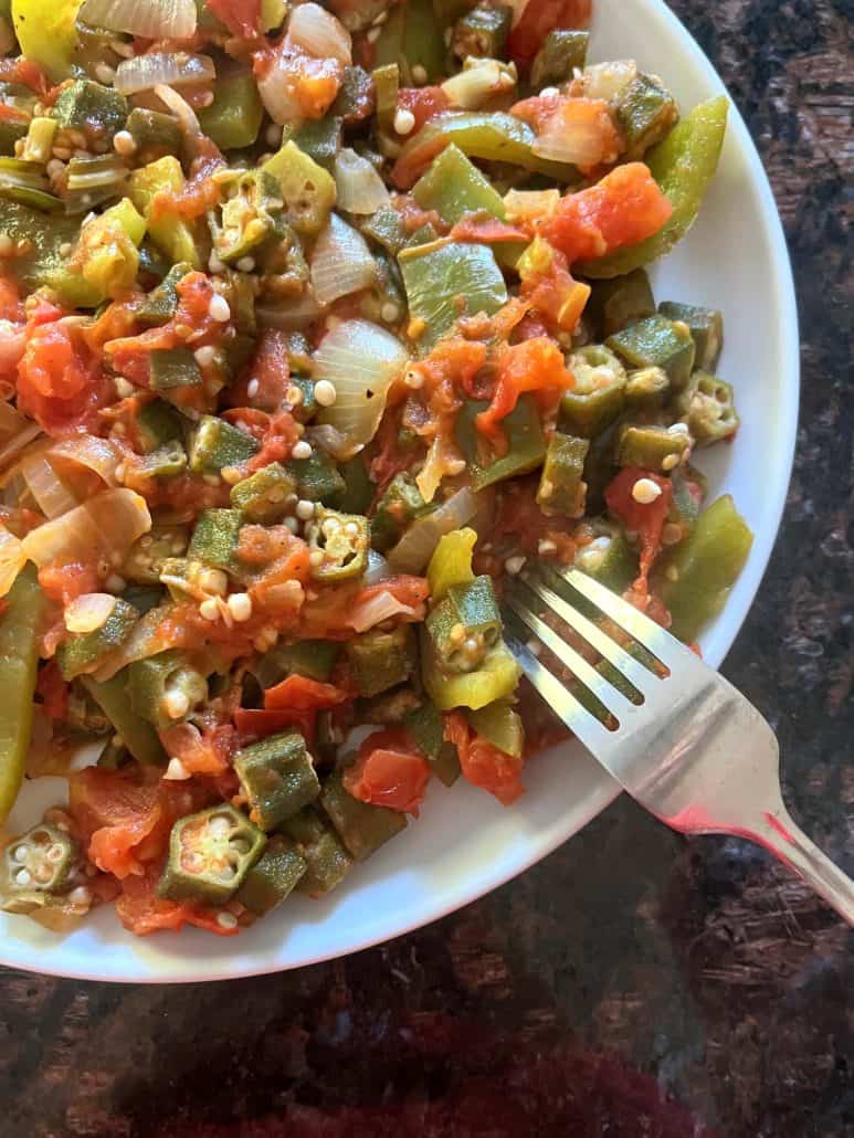 A plate of sautéed okra, tomatoes, bell peppers, and onions with a fork resting on the side.