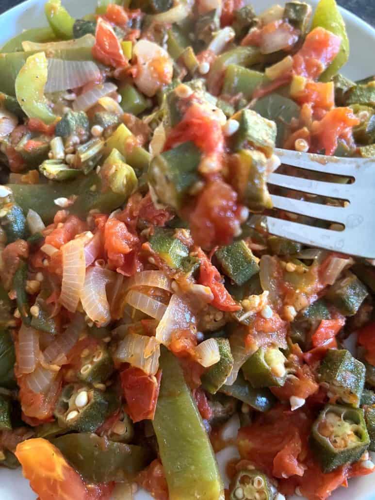 Close-up of a fork lifting a bite of sautéed okra, tomatoes, bell peppers, and onions, highlighting the tender and flavorful vegetables from the Okra and Tomatoes recipe.