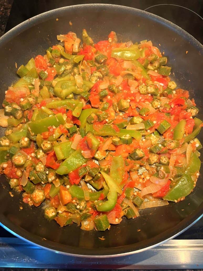 A top-down view of a frying pan filled with sautéed okra, tomatoes, bell peppers, and onions, creating a colorful and healthy Okra and Tomatoes dish.