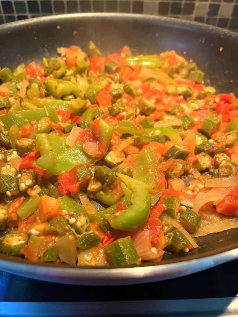 Close-up of a frying pan filled with sautéed okra, tomatoes, bell peppers, and onions.