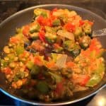 A close-up of a spoonful of sautéed okra, tomatoes, bell peppers, and onions in a frying pan, showcasing the vibrant colors and tender texture of this Okra and Tomatoes recipe.