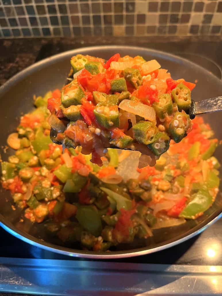 A close-up of a spoonful of sautéed okra, tomatoes, bell peppers, and onions in a frying pan, showcasing the vibrant colors and tender texture of this Okra and Tomatoes recipe.