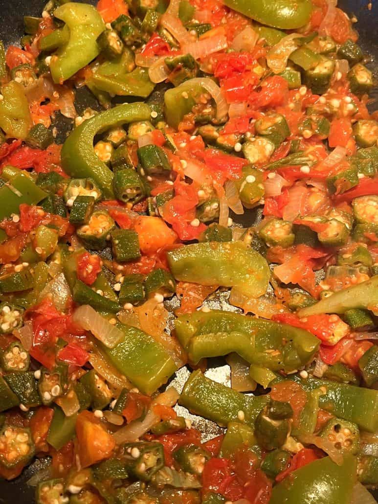 A close-up of sautéed okra, tomatoes, bell peppers, and onions in a frying pan.