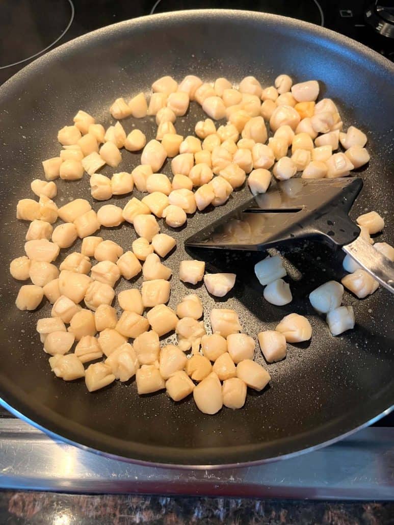 Bay scallops being stirred in a non-stick pan with a spatula.