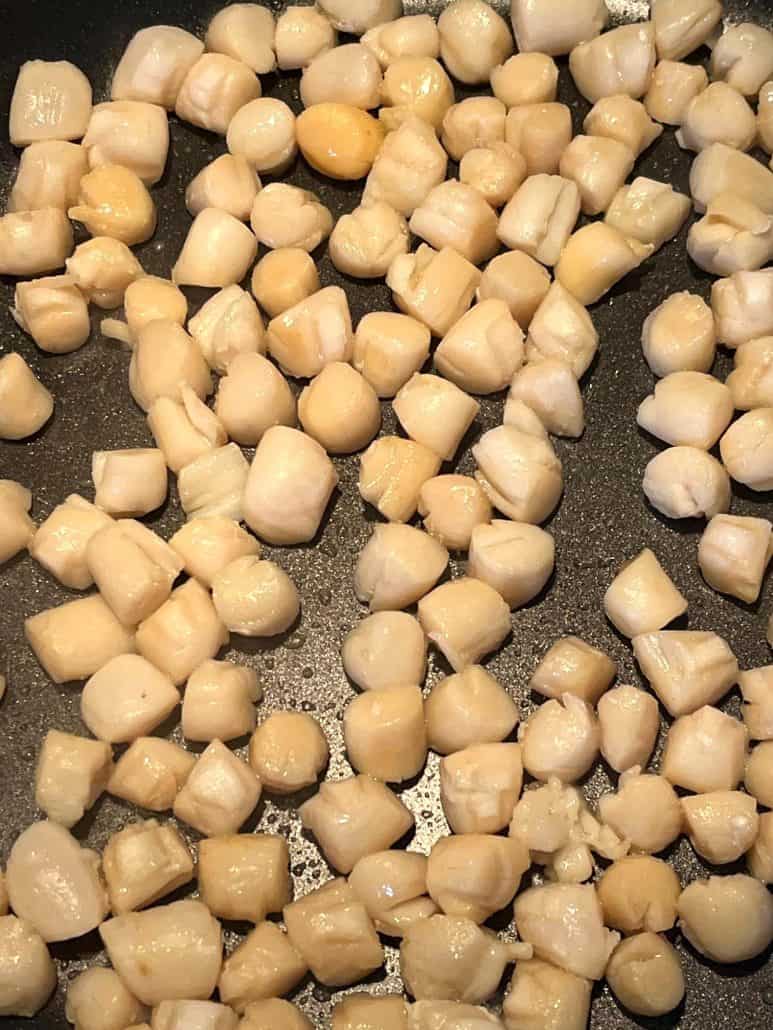 Close-up of bay scallops cooking in a pan, starting to turn opaque as they cook.