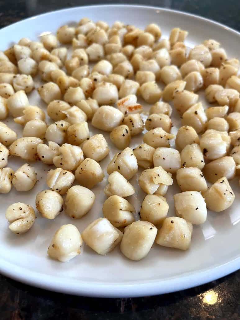 Cooked bay scallops seasoned with salt and pepper, served on a white plate.