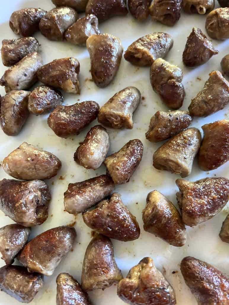 Close-up of pan-fried chicken hearts on a white plate, showing their crispy, golden-brown exterior after cooking.