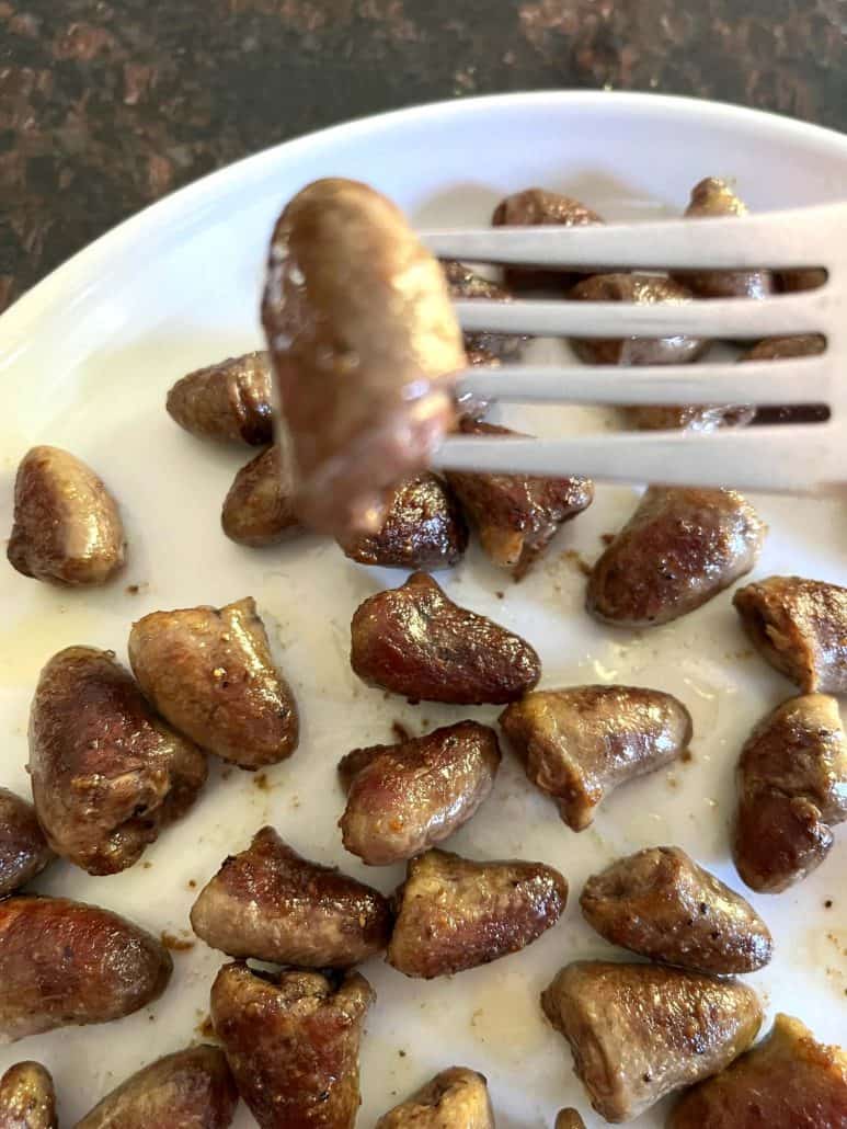 Close-up of a pan-fried chicken heart held by a fork over a plate of golden-brown chicken hearts, showcasing their tender and crispy texture