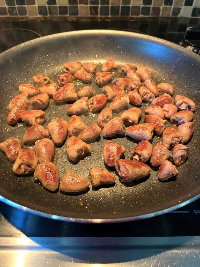 Pan-fried chicken hearts cooking in a non-stick skillet, browned and sizzling for a tender and flavorful dish.