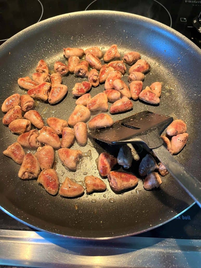 Chicken hearts being pan-fried in a non-stick skillet, with a spatula ready to stir them for even cooking and a crispy finish.