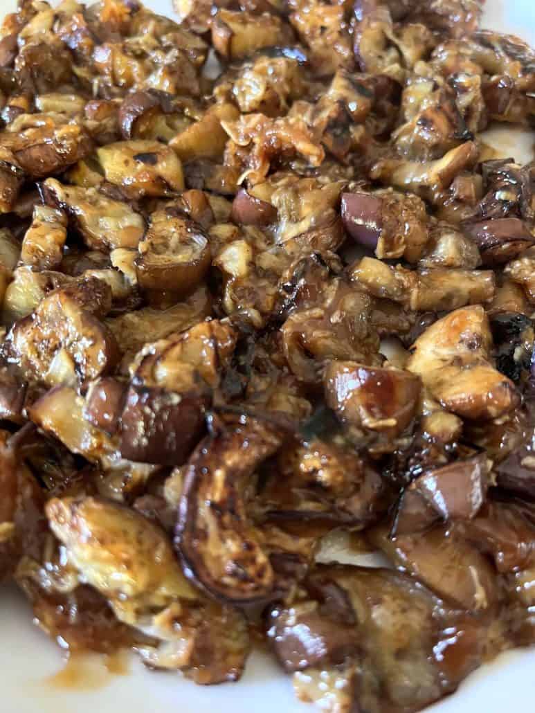 Close-up of a plate filled with caramelized pieces of pan-fried Chinese eggplant coated in a rich garlic sauce.