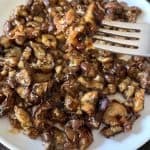 A fork holding a bite of pan-fried Chinese eggplant with garlic sauce above a plate, showcasing the tender, caramelized eggplant pieces coated in a flavorful sauce.