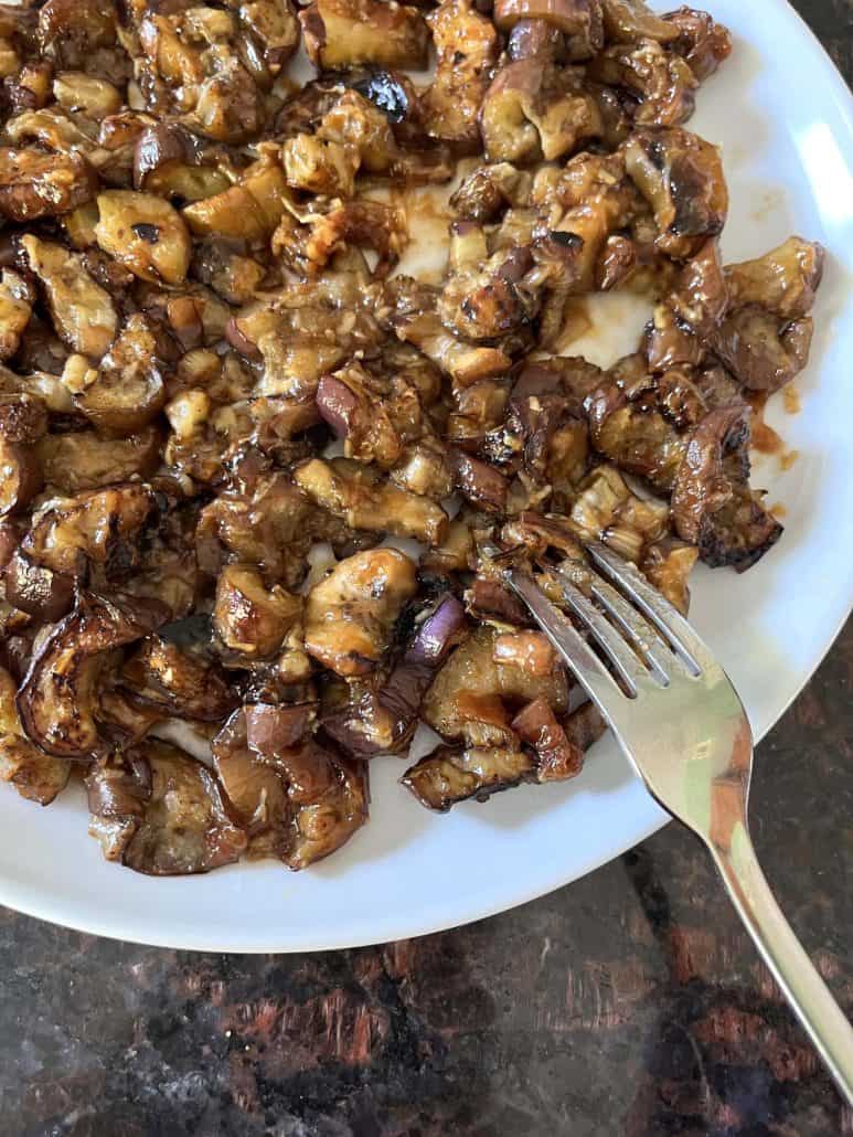 A plate of pan-fried Chinese eggplant with garlic sauce, featuring tender, caramelized pieces of eggplant, with a fork ready to serve.