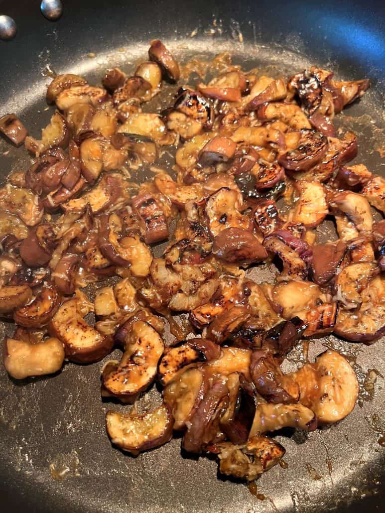 Pan-fried Chinese eggplant pieces sizzling in a skillet, coated in a thick, glossy garlic sauce, showing the rich caramelization and savory texture of the dish.