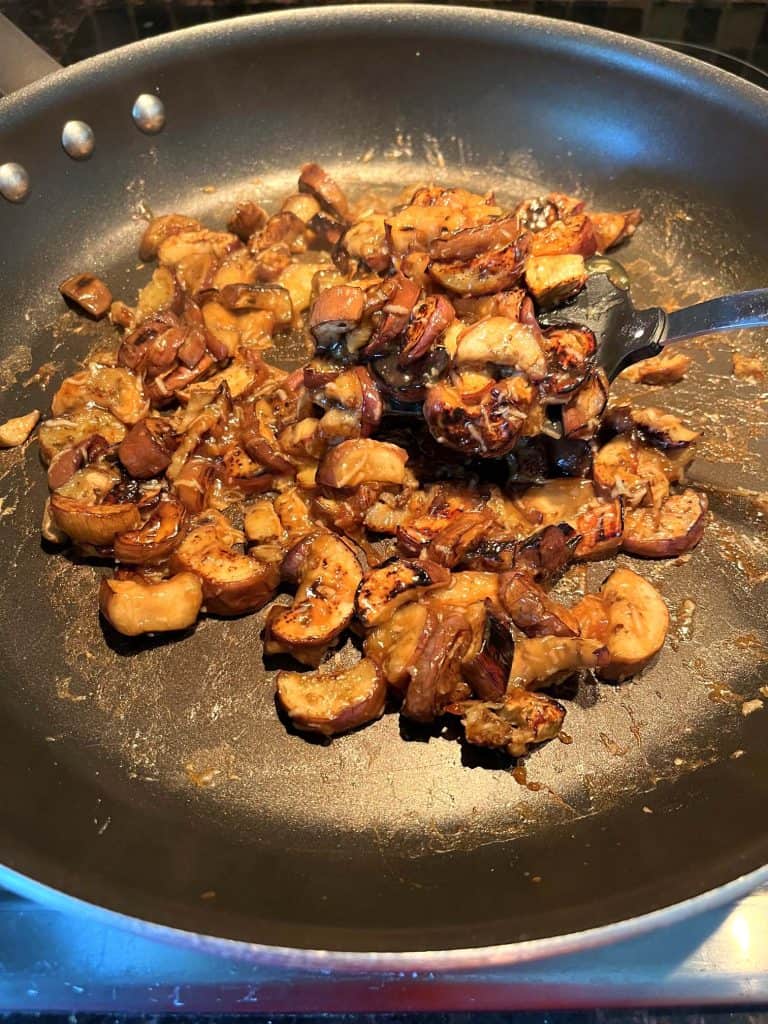 Pan-fried Chinese eggplant cooking in a large skillet, with a spatula lifting a portion of the caramelized eggplant pieces coated in a savory garlic sauce.