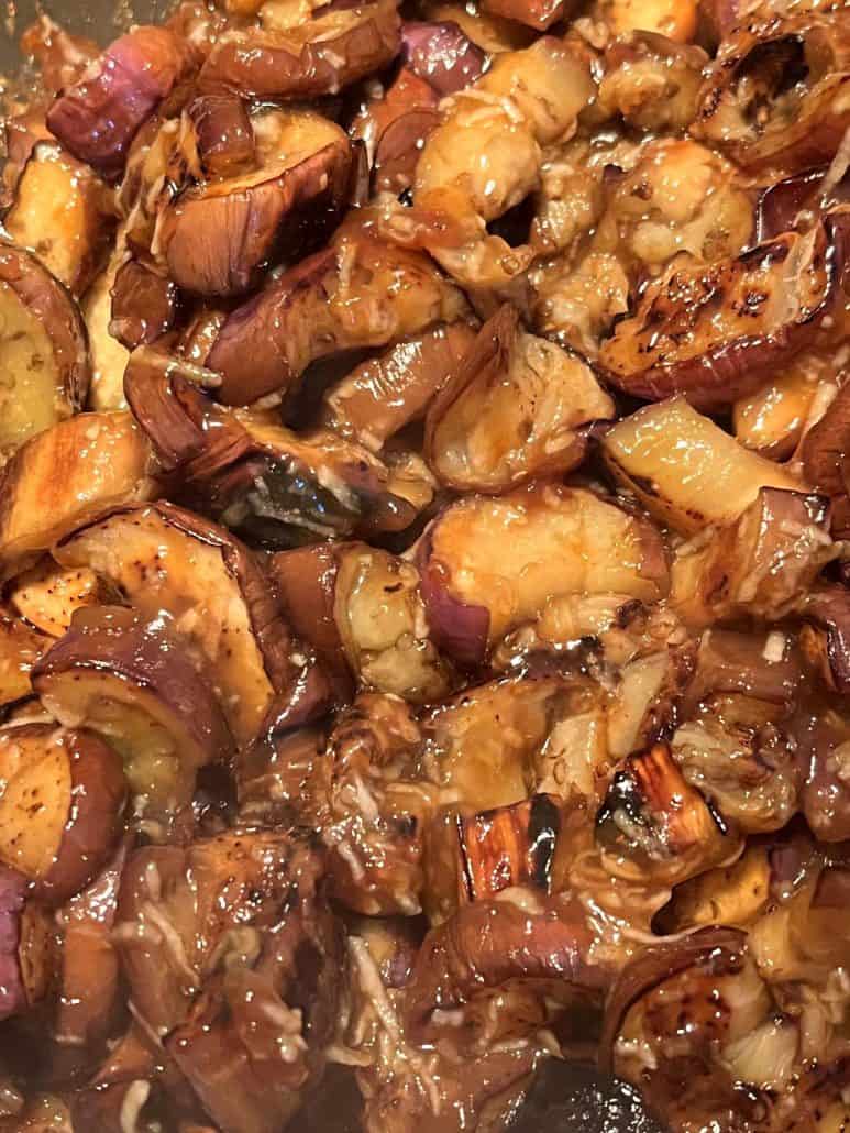 Close-up view of cooked Chinese eggplant pieces coated in a thick, glossy garlic sauce, showcasing their rich color and caramelized texture.