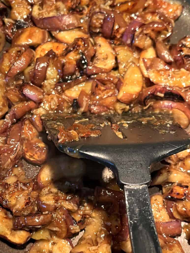 Close-up of pan-fried Chinese eggplant in a skillet, coated with a thick garlic sauce, being stirred with a spatula to ensure even cooking and flavor distribution.