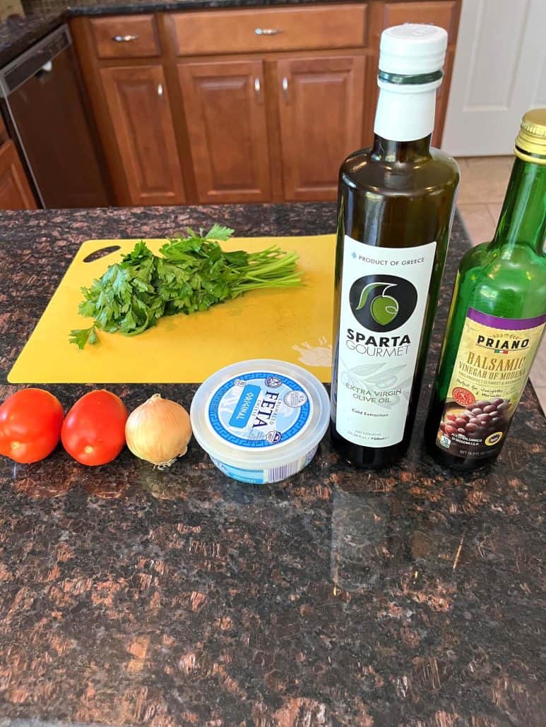 Ingredients for a parsley salad, including fresh parsley, tomatoes, onion, feta cheese, olive oil, and balsamic vinegar.