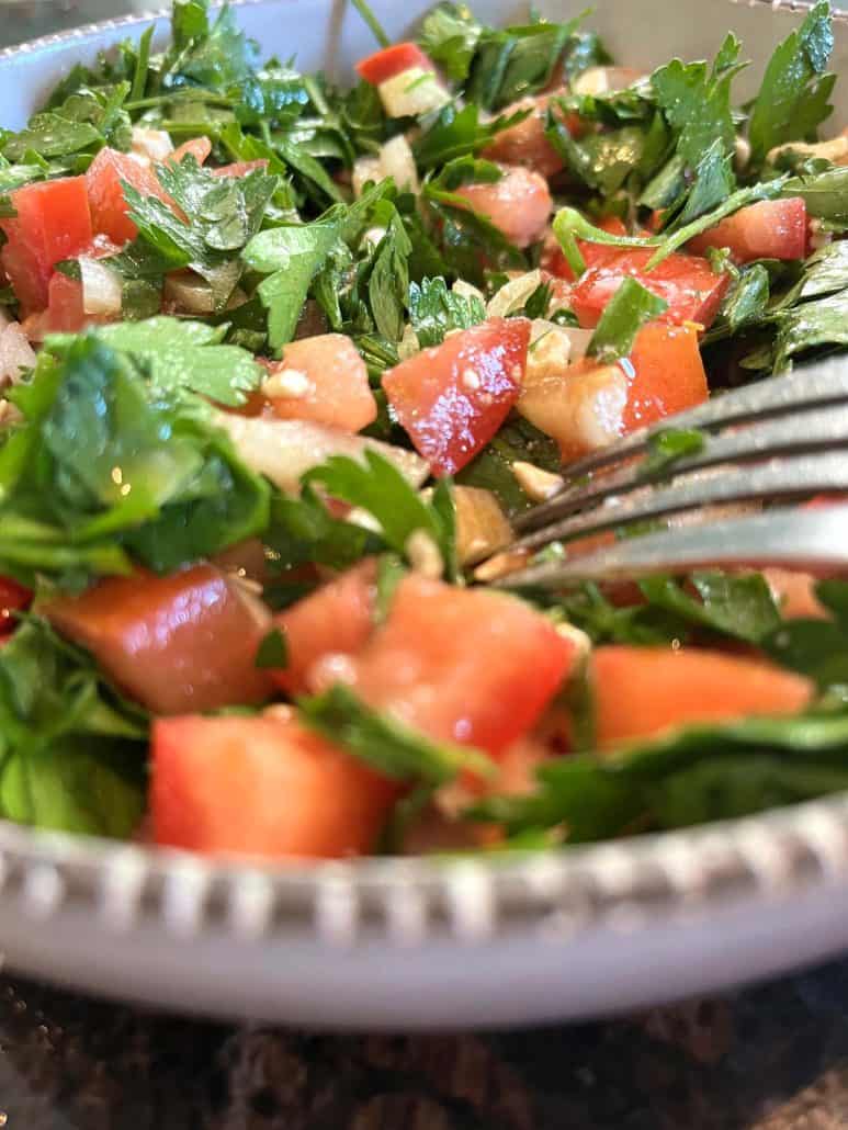 Close-up of parsley salad with diced tomatoes, onions, and feta cheese, with a fork resting in the bowl, highlighting the fresh ingredients. ready to enjoy!